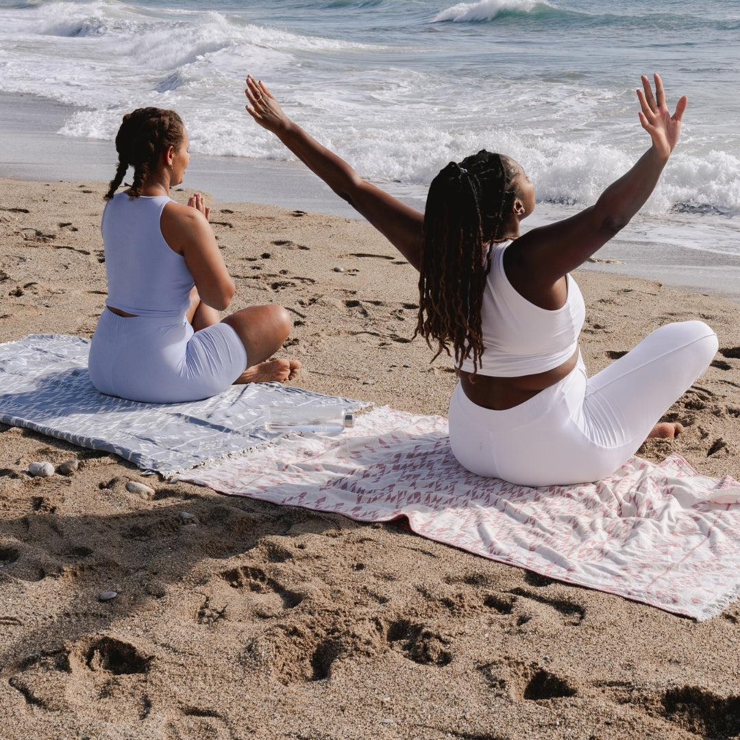 Two women practicing yoga on a beach with ocean waves in the background