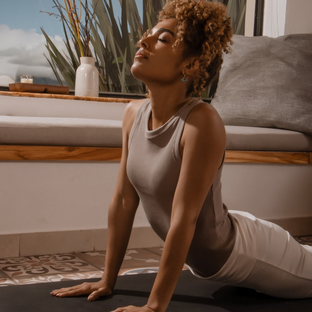 Woman practicing yoga on a mat in a serene indoor setting with plants and a couch.