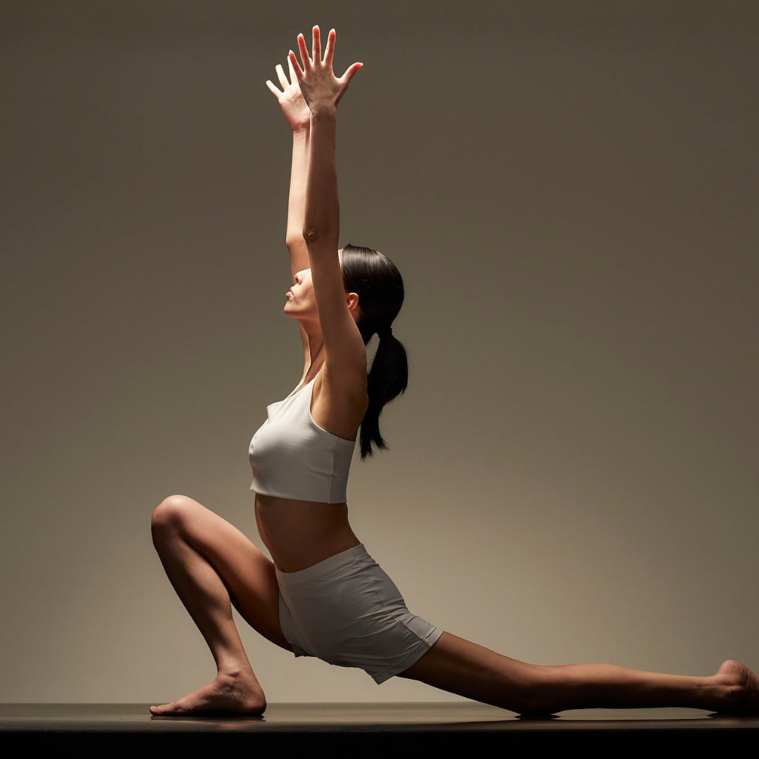 Woman performing a yoga pose with one arm raised against a neutral background