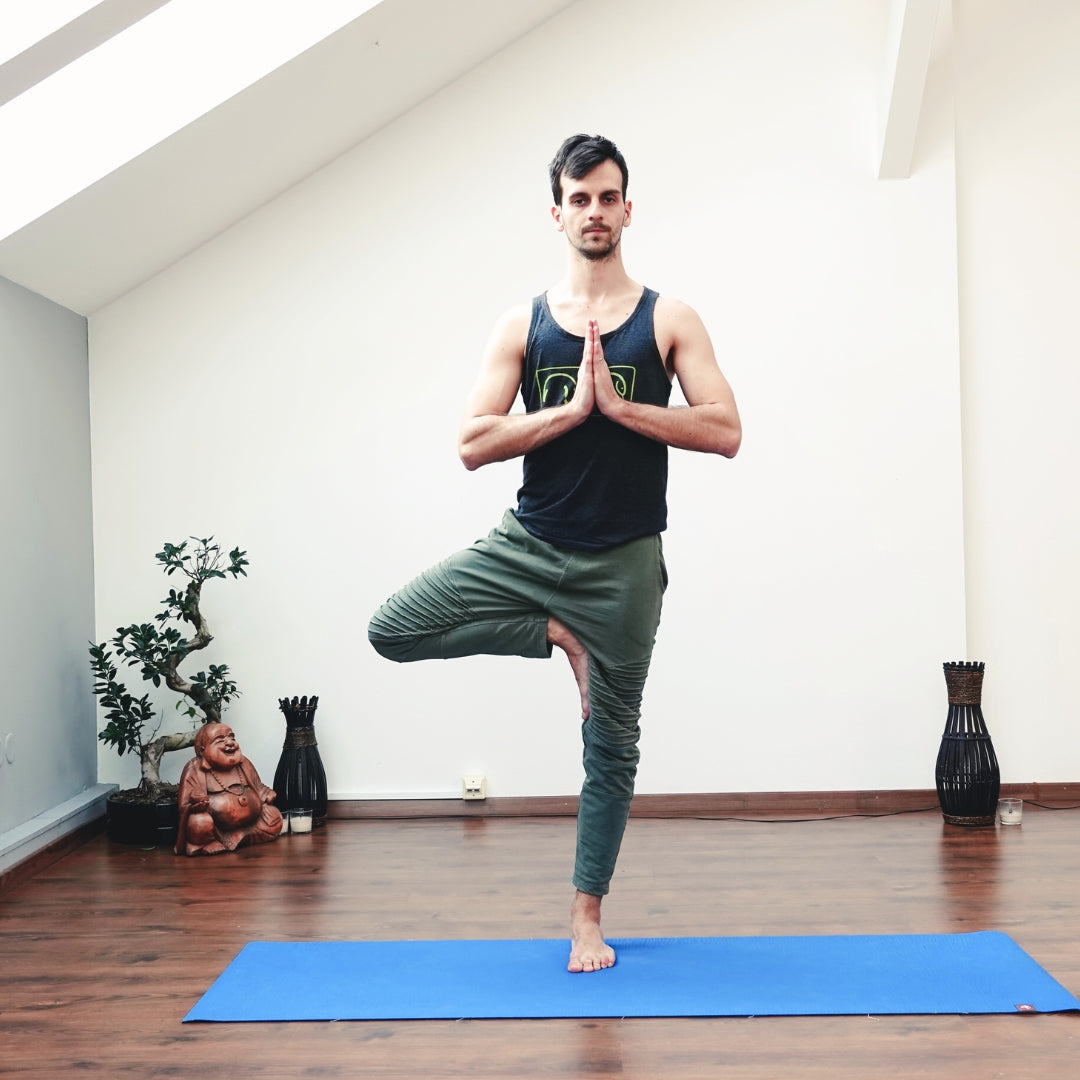 Man practicing yoga in a room with plants and a Buddha statue.